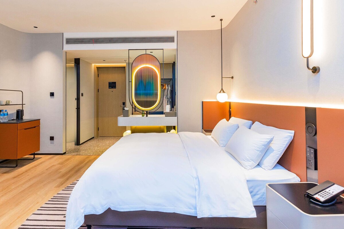 A hotel room with a bed, bedside table, and a mirror.