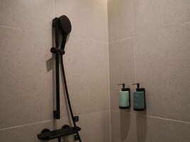 Ducha con mando de mano y panel empotrado. Dos botellas de champú y acondicionador en la pared.