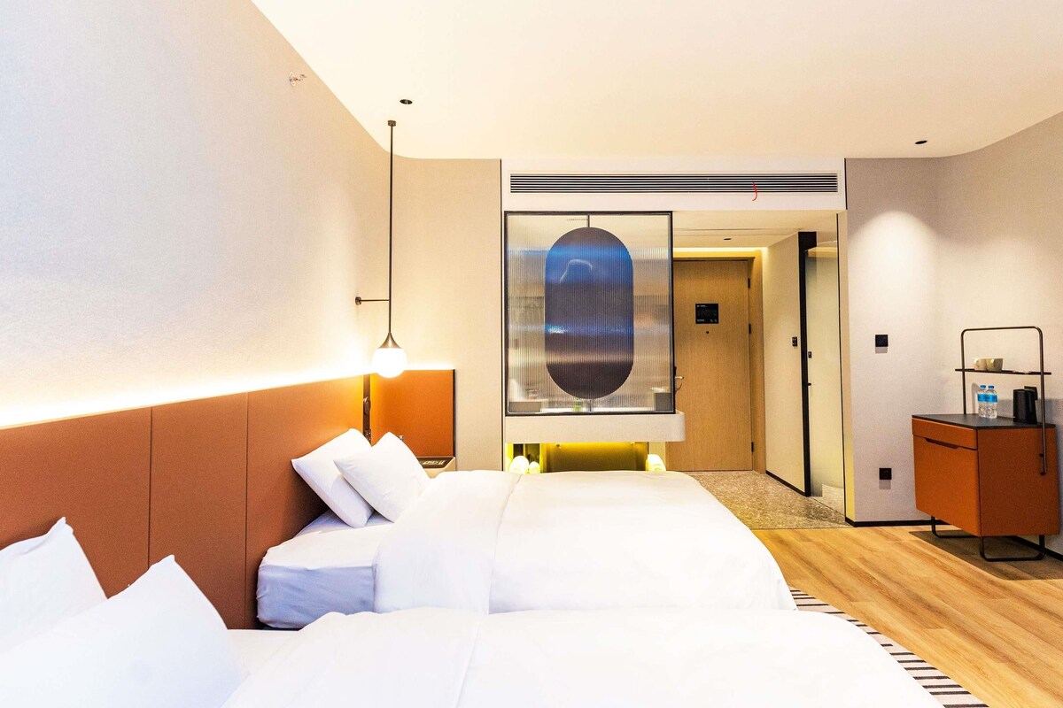 A hotel room with a bed, bedside lamp, and a view of the hallway.
