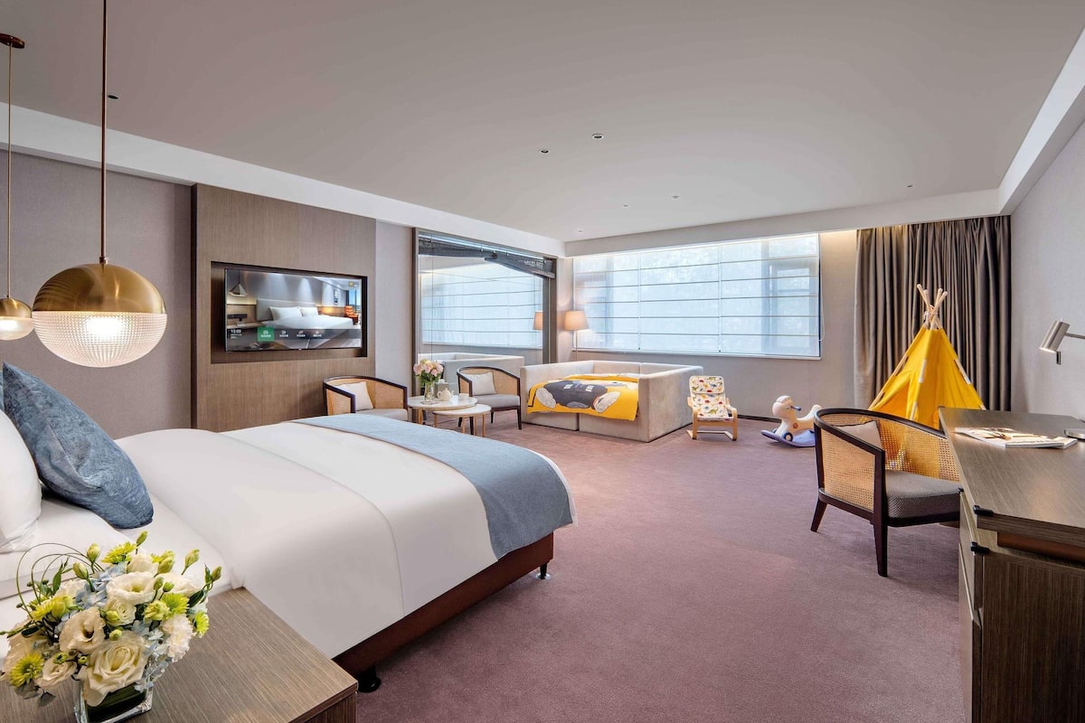 Ein modernes Hotelzimmer mit Bett, Sofa, Fernseher und einer kleinen Essecke.