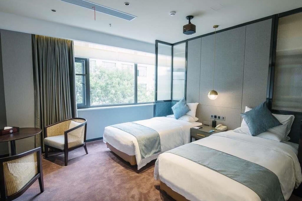 A hotel room with two beds, a desk, a chair, and a large window.