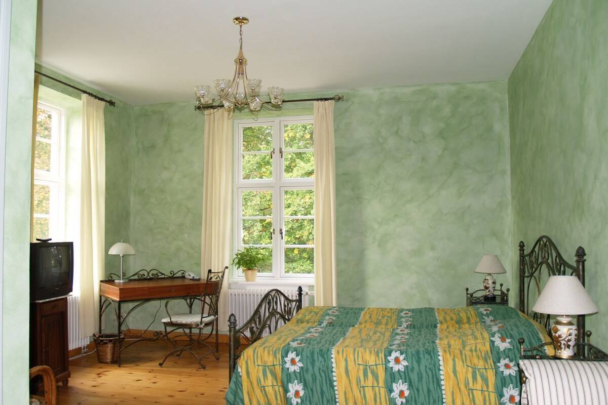 Un dormitorio con cama, escritorio, silla, televisor y ventana con cortinas.