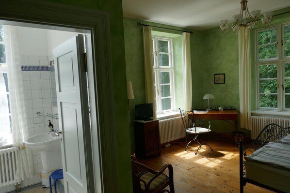 Een kamer met houten vloer, een bed, een bureau met stoel, een radiator en een raam met gordijnen.