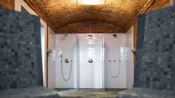 A shower area with a brick ceiling, white tiled walls, and a tiled floor.