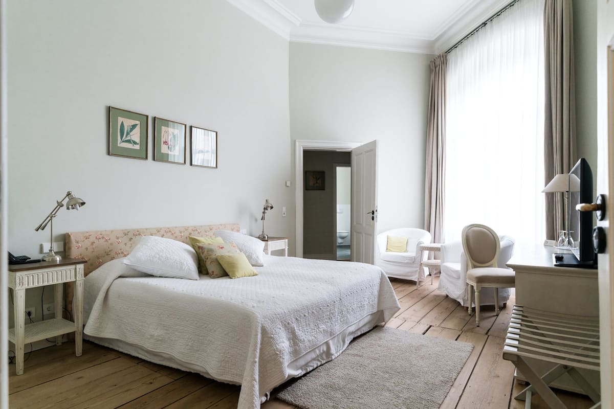 Une chambre bien éclairée, avec un grand lit, des tables de chevet, une chaise et un téléviseur.