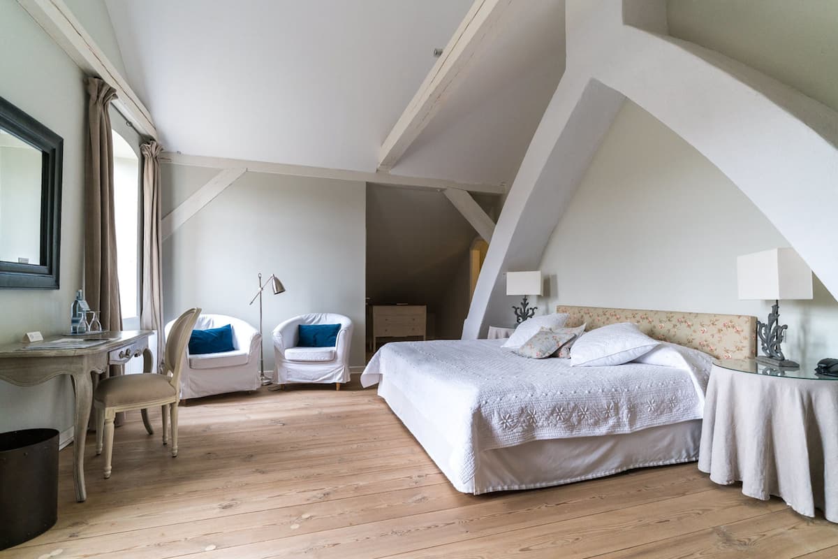 Une chambre à coucher avec un grand lit, deux chaises, un bureau et une table de chevet.