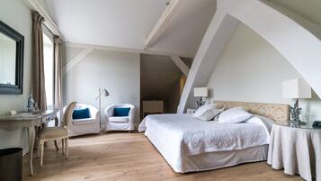 Een slaapkamer met een groot bed, twee stoelen, een bureau en een nachtkastje.