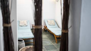 A room with two beds, each with a pillow and a small table. The room has a tiled floor and white walls.
