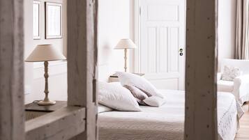 A bedroom with a bed, two bedside lamps, a door, and a white chair.