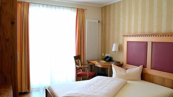 A hotel room with a bed, a desk with a chair, a telephone, and a window with curtains.