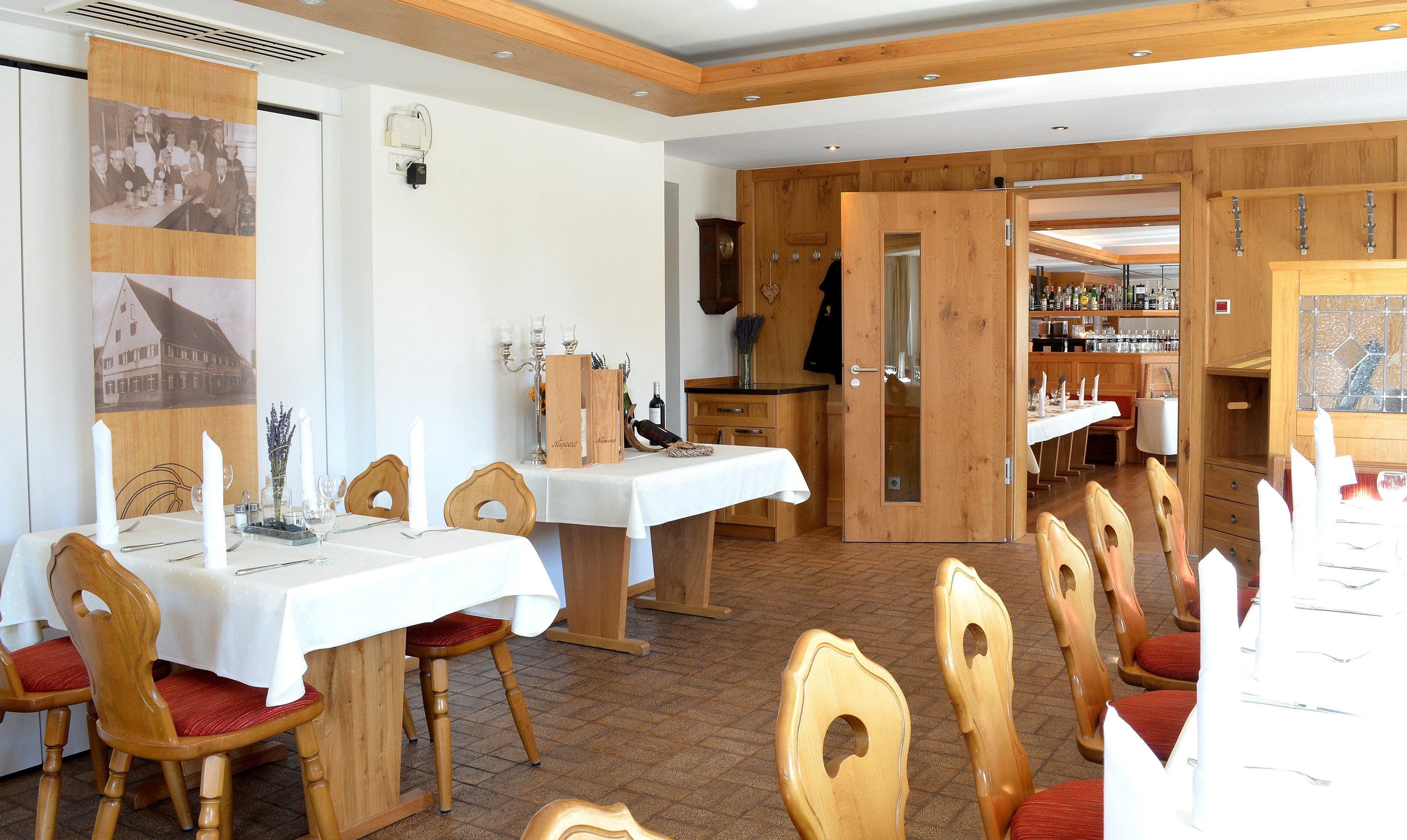 Zona pranzo con tavoli e sedie in legno, angolo bar con bottiglie e un orologio appeso al muro.