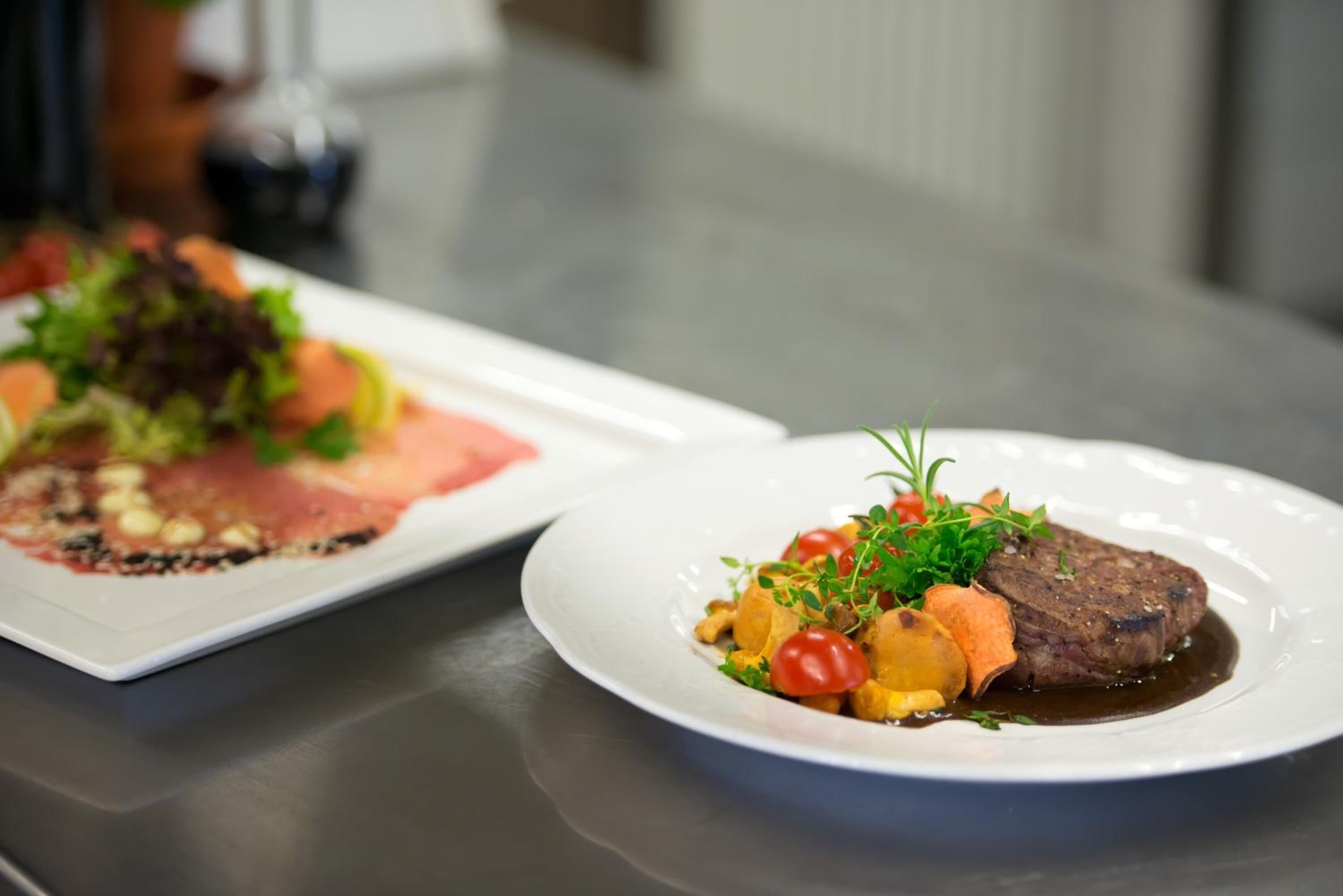 Una mesa de comedor con dos platos de comida, uno con un filete y verduras, y otro con un plato diferente.
