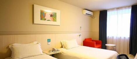 A hotel room with two beds, a small table, a chair, an air conditioning unit, and a painting on the wall.