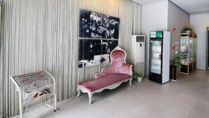 Un hall d’entrée moderne avec un canapé en velours rouge, un présentoir à magazines, une grande peinture abstraite et un distributeur automatique.