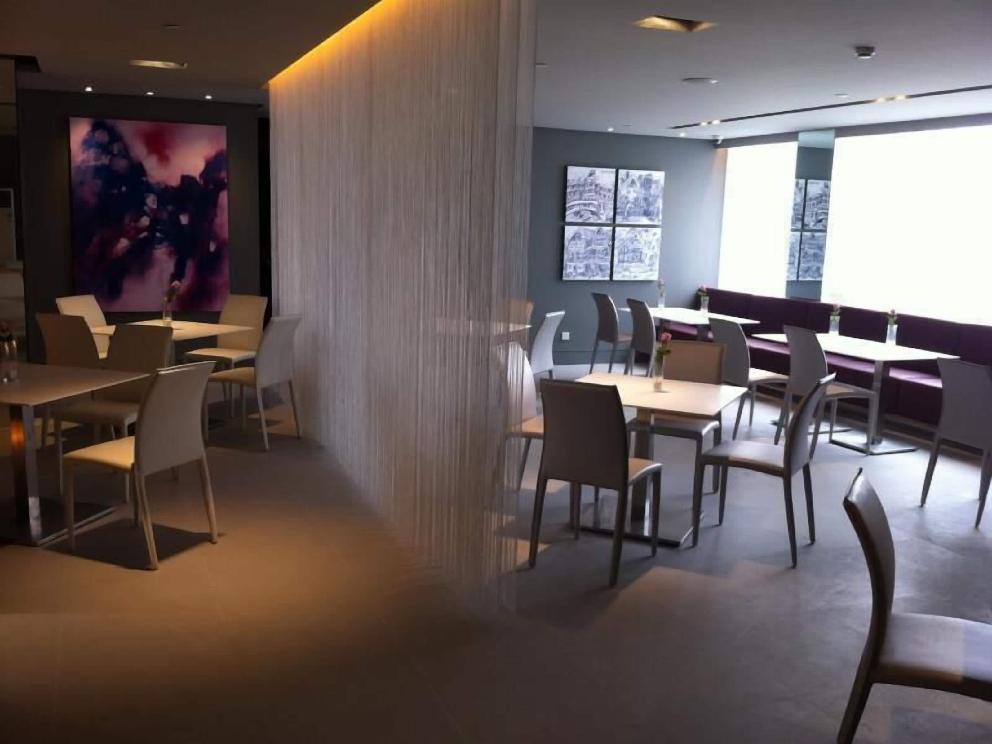 A modern dining area with tables and chairs, a large abstract painting on the wall, and a window with a view.