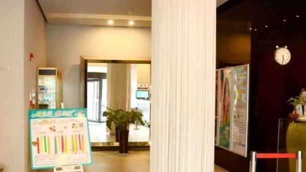 Un hall d’hôtel avec une grande colonne blanche, un comptoir d’accueil, une horloge au mur et une plante au centre.