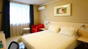 Une chambre d’hôtel avec un lit, une chaise rouge, une petite table et un tableau accroché au mur.