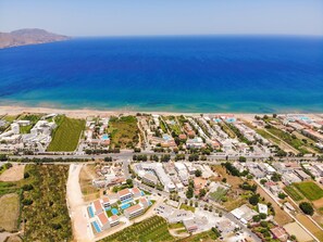 An aerial view of a coastal resort with multiple buildings, a beach, and a clear view of the ocean. - Vantaris Blue - Adults Only (Apokoronas)