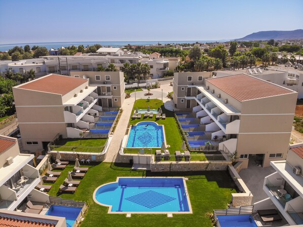 A hotel with a central swimming pool, multiple balconies, and a view of the sea. - Vantaris Blue - Adults Only (Apokoronas)