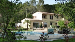 Una casa de dues plantes amb piscina, envoltada de vegetació i arbres.