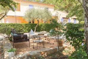 An outdoor patio with a sofa, chairs, and a table, surrounded by potted plants and a stone pathway. - La Maison de la Cigale (Forcalqueiret)