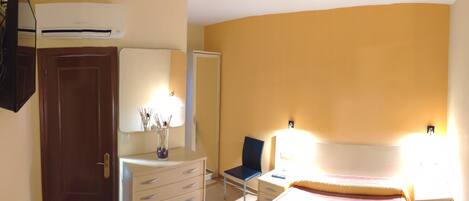 Un dormitorio con cama, una silla, cómoda, espejo y aire acondicionado instalado en la pared.