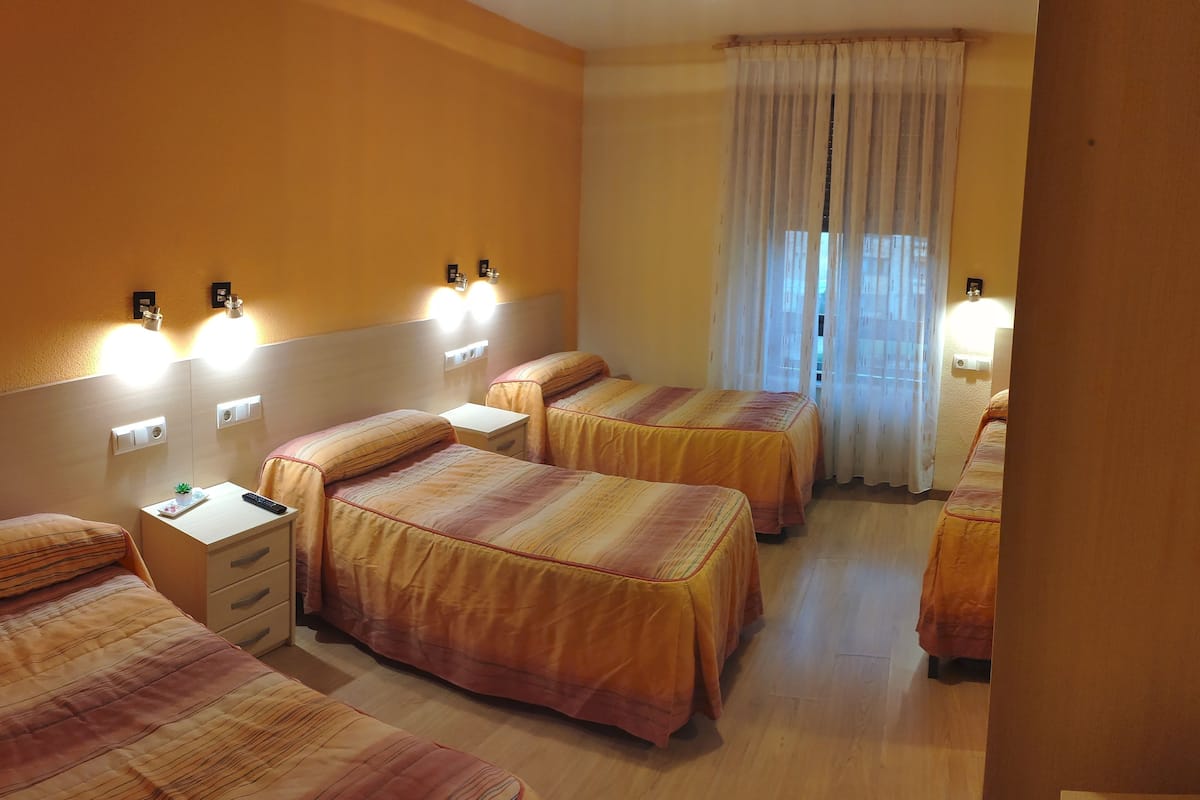 Une chambre d’hôtel avec quatre lits, chacun recouvert d’une courtepointe à rayures, une table de chevet avec une lampe et une petite plante.