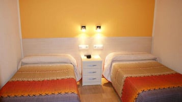 A room with two single beds, a small white nightstand with drawers, and two wall-mounted light fixtures.