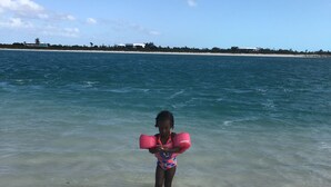 Un niño parado en aguas poco profundas en una playa, con cielo despejado.