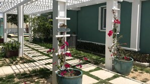 Un área de patio techada con una estructura de pérgola, plantas en macetas y un letrero de bienvenida.