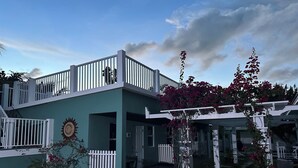 Un edificio de dos pisos con un balcón, un reloj de sol y macetas con plantas.
