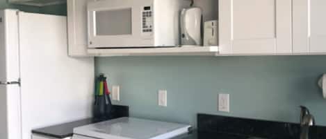 A kitchen with white cabinets, a microwave, a stove, and a sink.