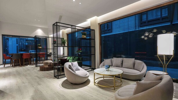 Een moderne woonkamer met een bank, fauteuils en een salontafel. Er is een eethoek met stoelen en een tafel. De kamer heeft grote ramen en uitzicht op de stad.