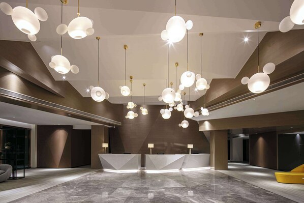 Un hall d’entrée moderne doté d’un comptoir de réception, d’un sol en marbre et de luminaires suspendus sphériques originaux.