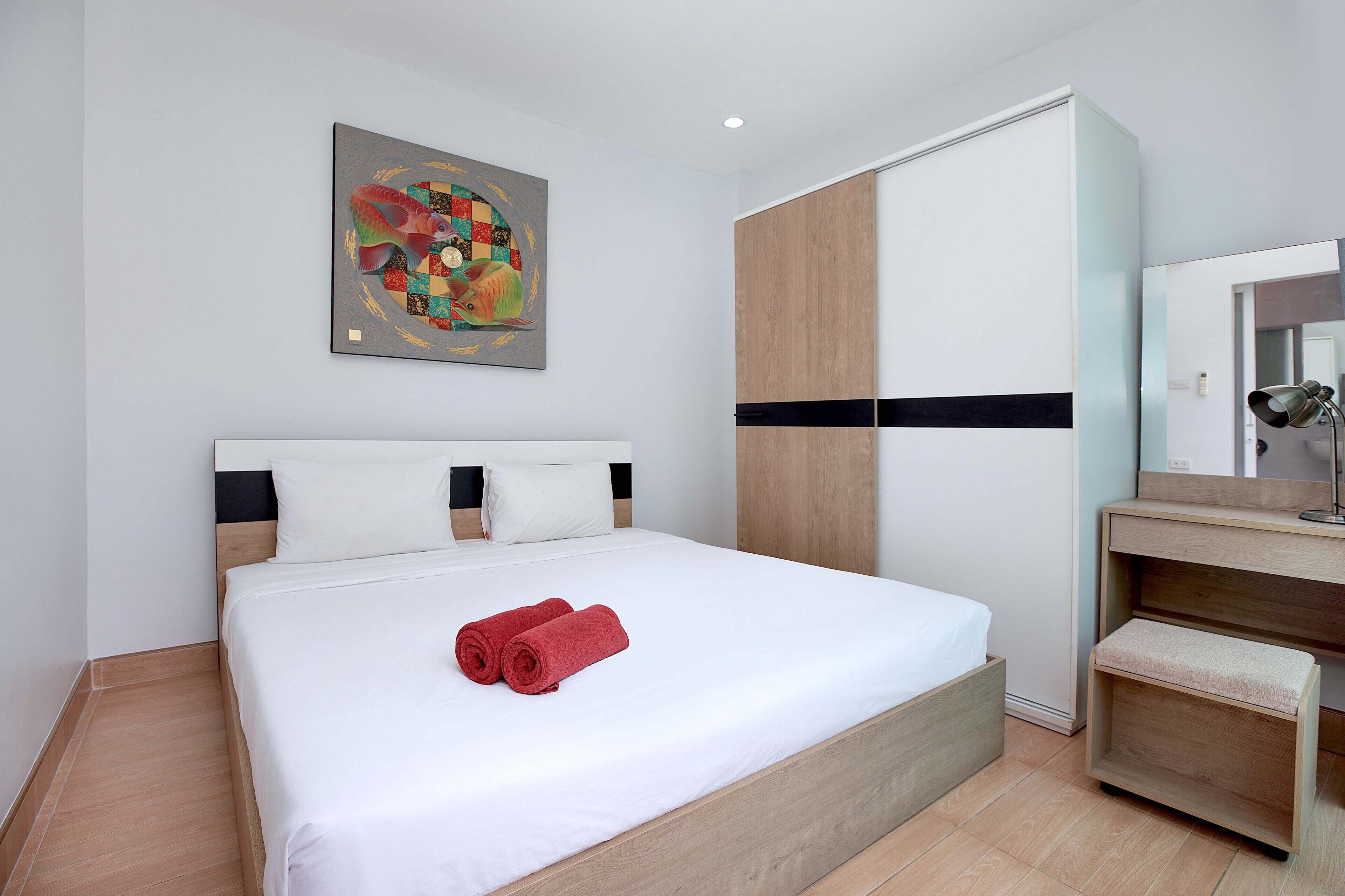 A modern hotel room with a large bed, a wooden wardrobe, a bedside table, and a painting on the wall.