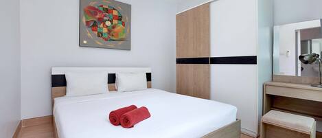 A modern hotel room with a large bed, a wooden wardrobe, a bedside table, and a painting on the wall.