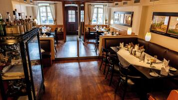 A restaurant with wooden floors, tables set for dining, and a bar area with bottles.
