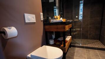 Ein modernes Badezimmer mit Toilette in Weiß, einem Holzwaschtisch, einer Duschkabine aus Glas und einem dunklen Fliesenboden.