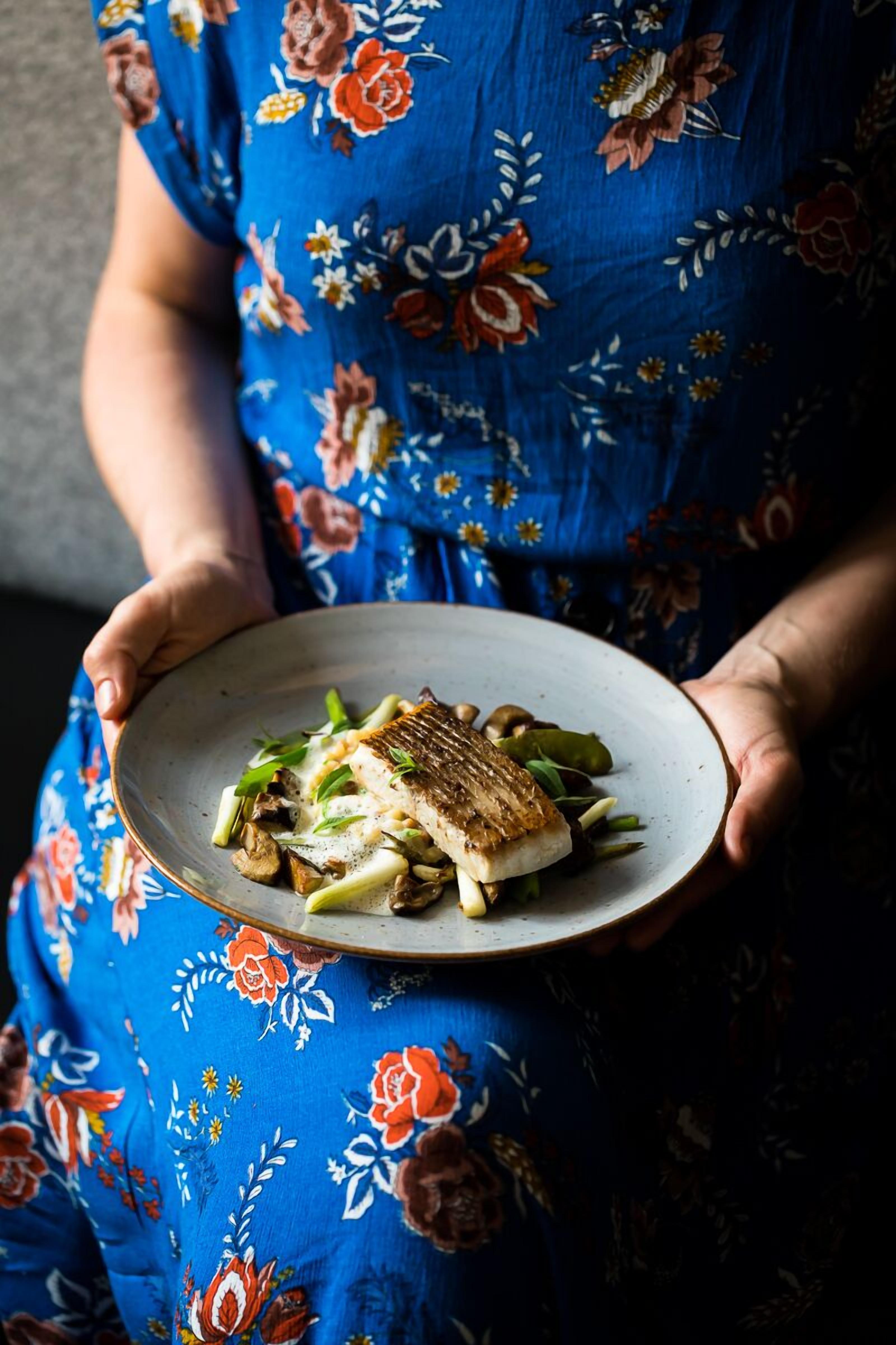 A person holding a plate with grilled fish and vegetables.
