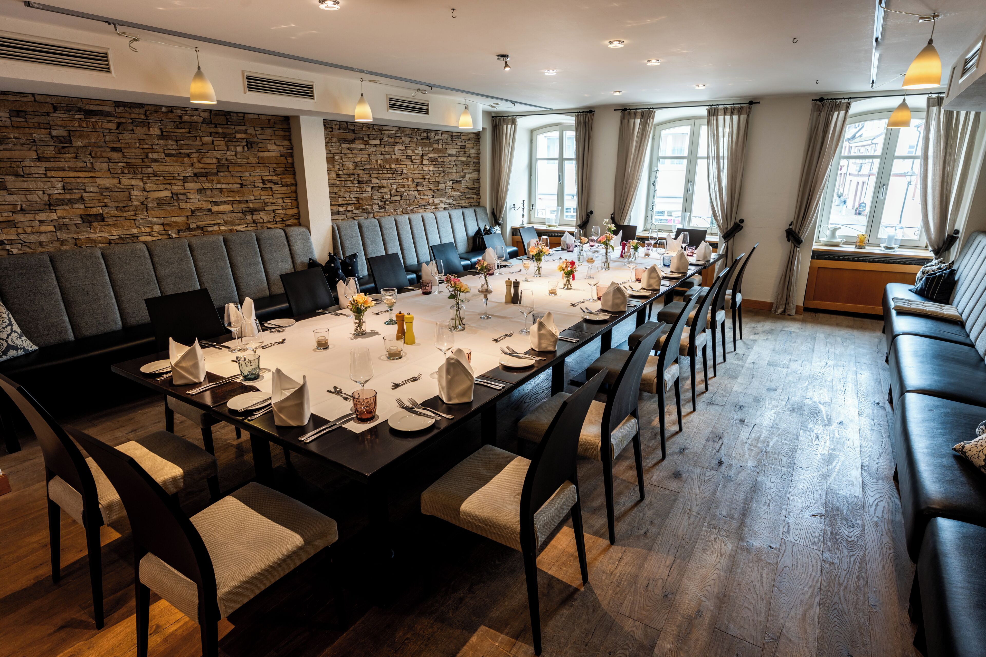 Una larga mesa de comedor lista para una comida en una habitación moderna con pared de piedra, suelo de madera y un sofá.