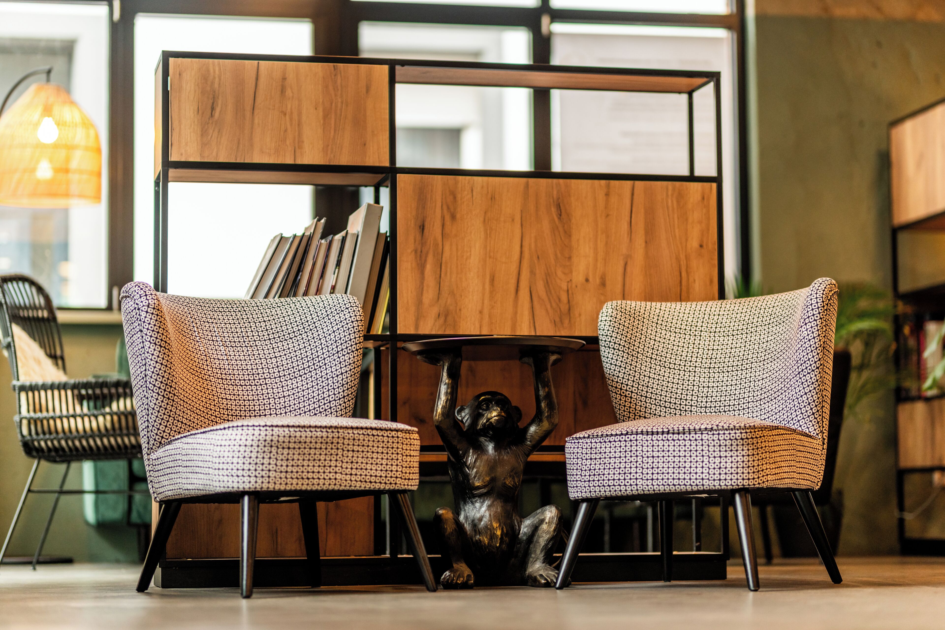 A modern interior with two patterned chairs, a wooden bookshelf, and a decorative monkey sculpture.
