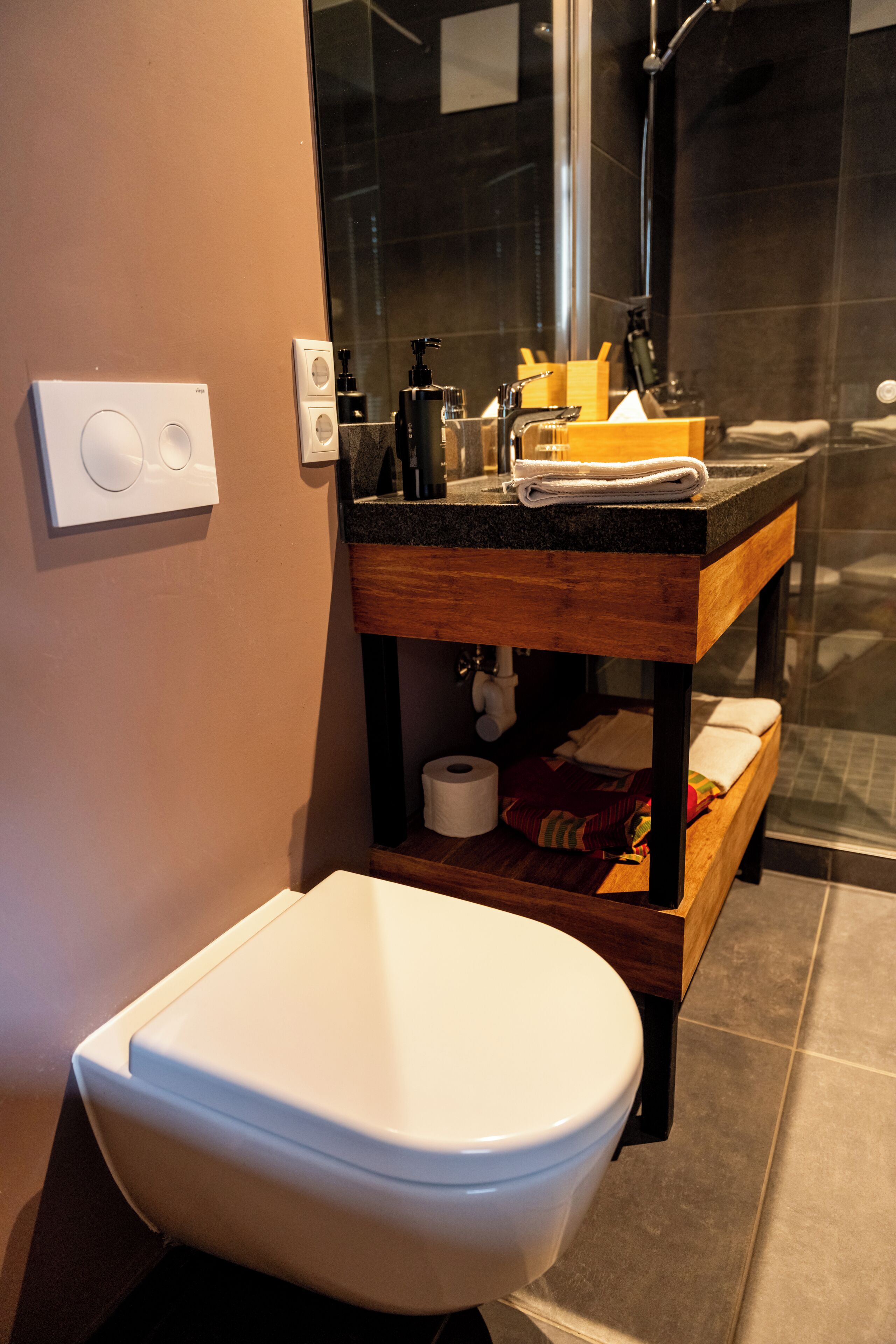 Un baño con inodoro, tocador de madera, espejo y zona de ducha.