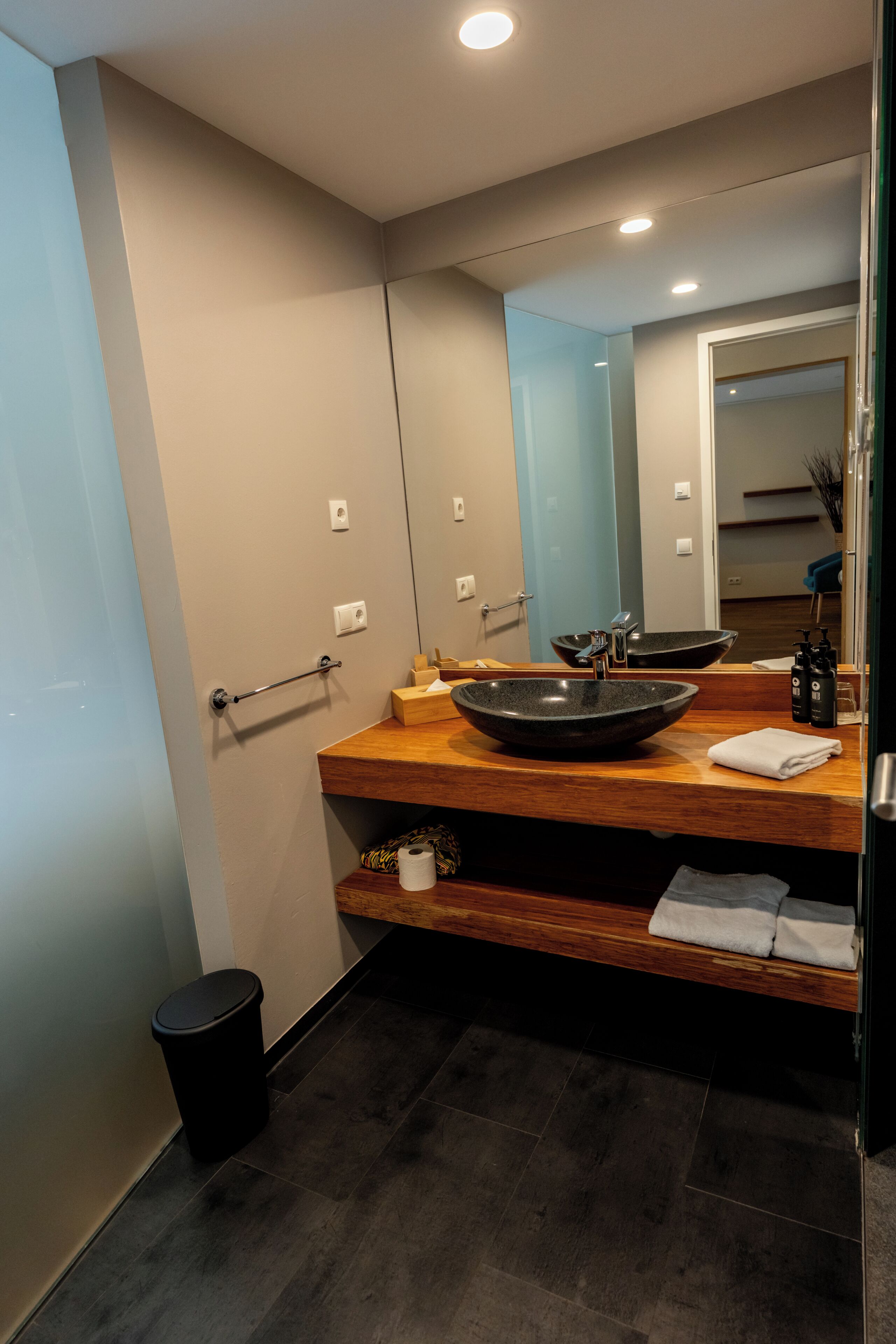 A modern bathroom with a wooden vanity, a large mirror, and a black vessel sink.