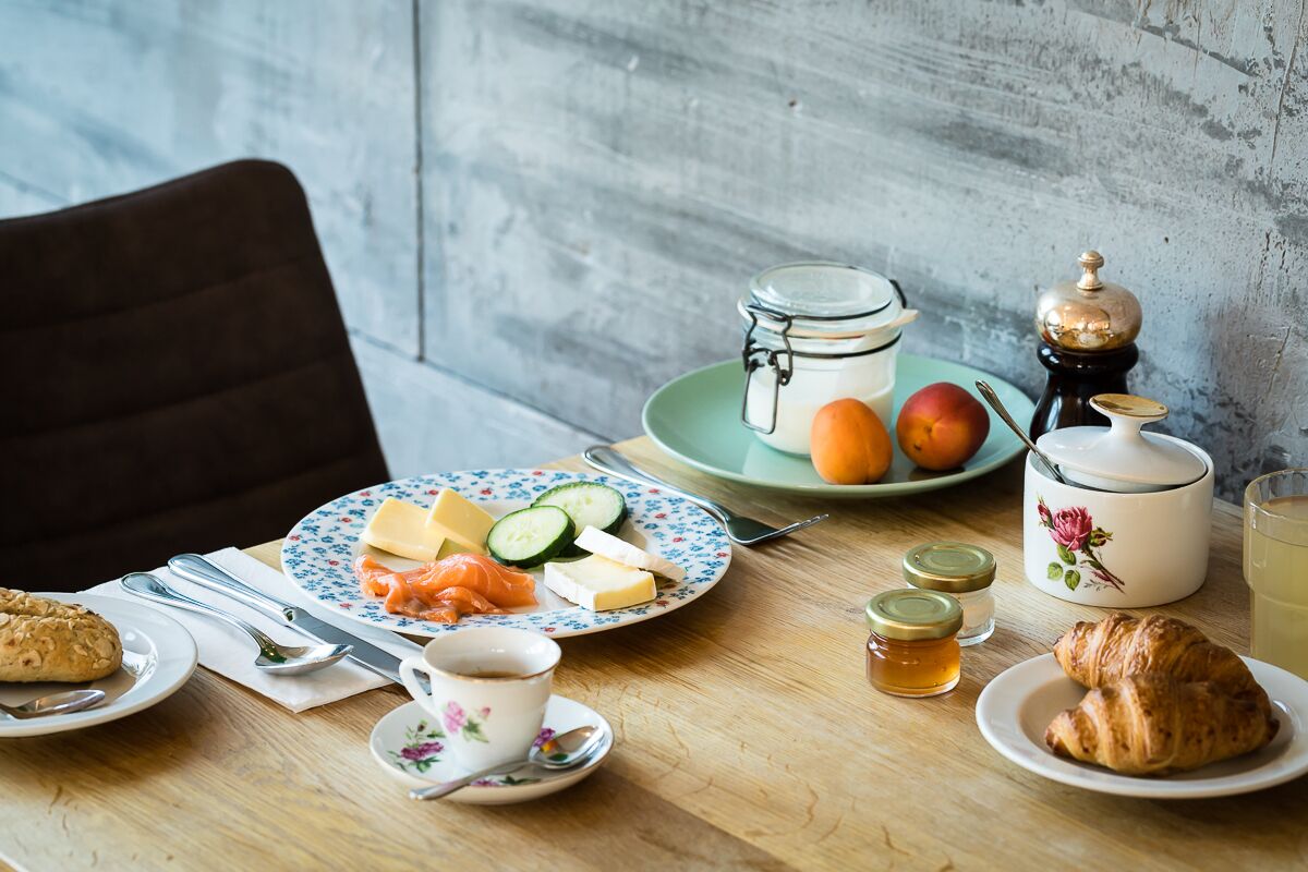 Mesa de café da manhã com pratos de comida, um bule, uma xícara e um pote de mel.