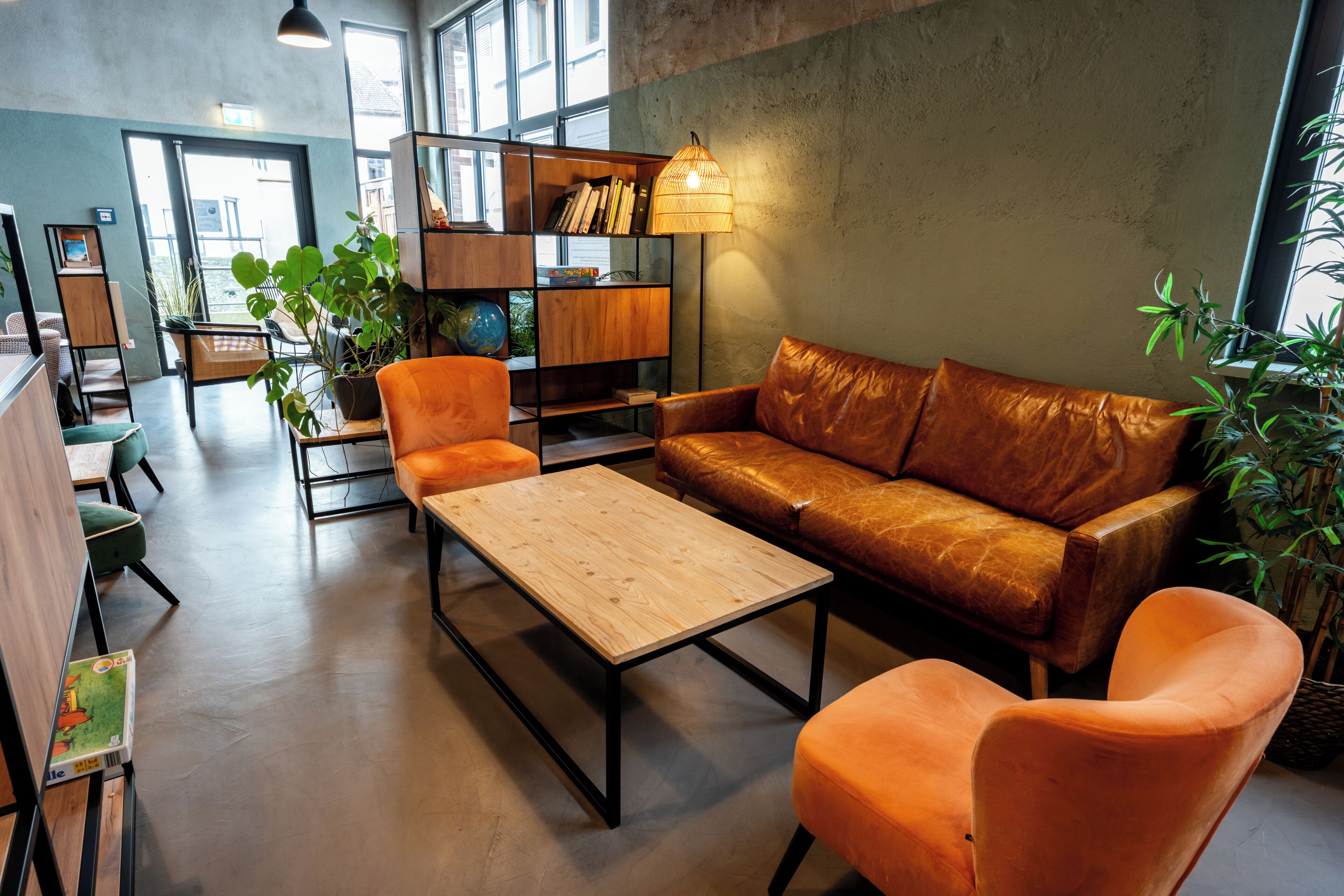 Ein moderner Loungebereich mit einer Ledersofa, orangefarbenen Ohrensesseln, einem Holztisch und einem Bücherregal.