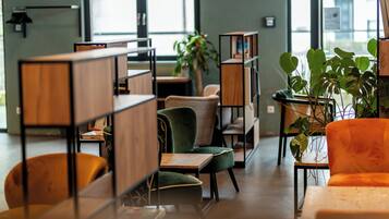 Un espace intérieur moderne, doté de meubles en bois, de chaises vertes et oranges, et de plantes en pot.