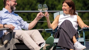 Two people toasting with wine glasses on a bench with a castle in the background. - Restaurant Hotel Zum Storchen (Waldkirch)