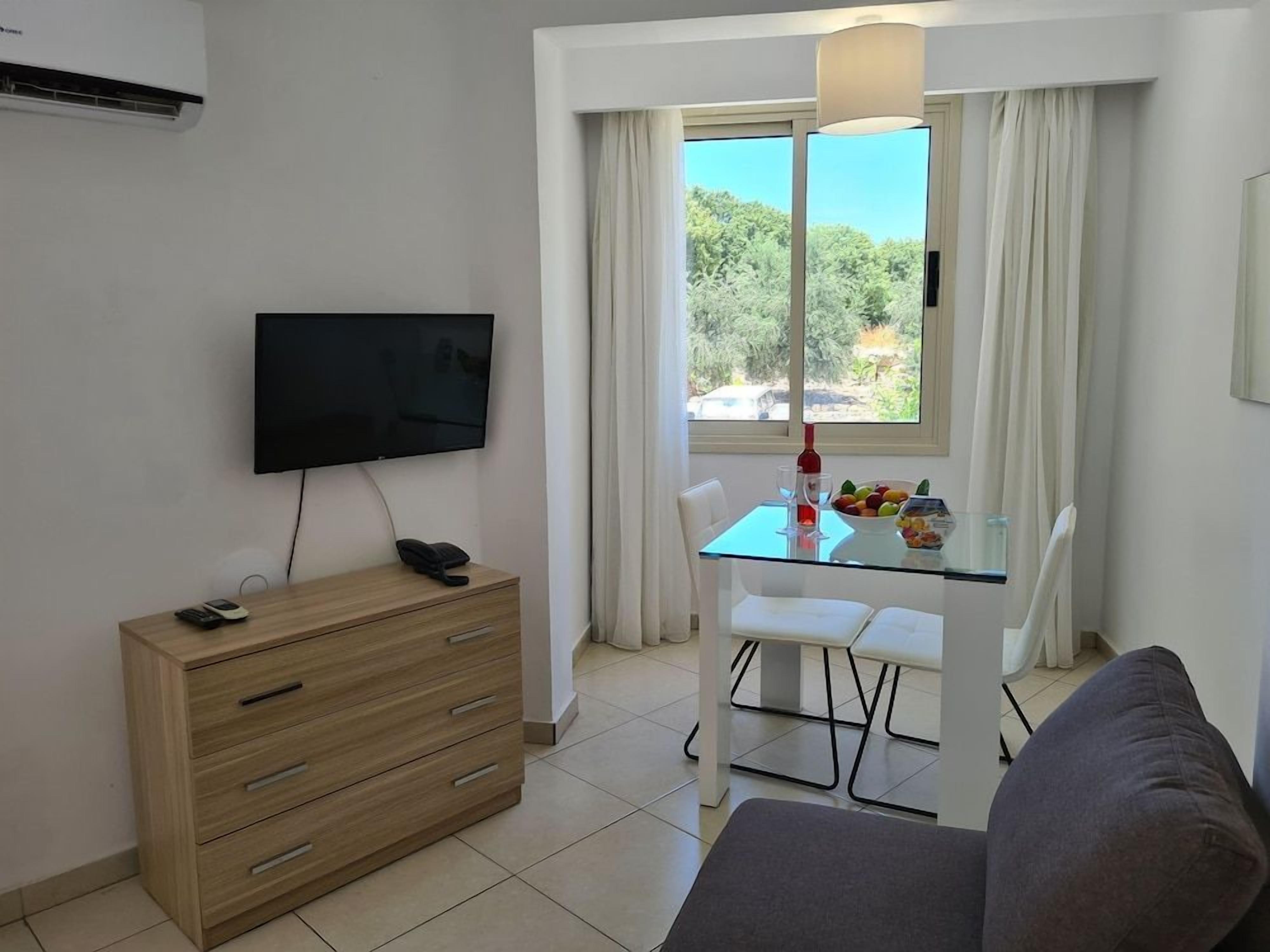 Una sala moderna con una televisión de pantalla plana, un aparador de madera, una mesa de comedor de vidrio con sillas y un sofá.
