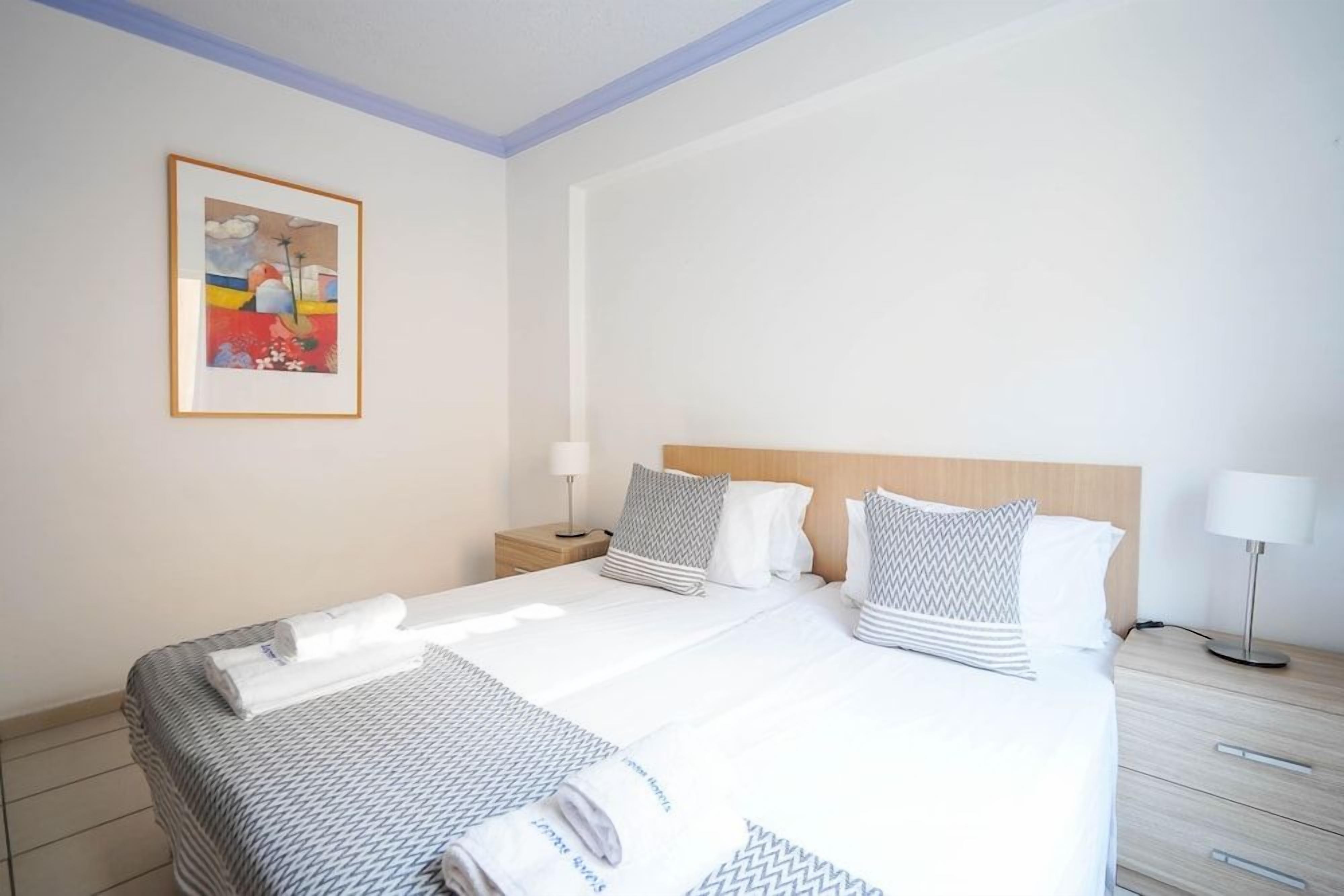 A hotel room with a bed, a nightstand, a lamp, and a framed picture on the wall.