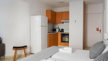 Una habitación de hotel compacta con kitchenette, una cama y toallas dobladas con cuidado, además de un taburete pequeño.
